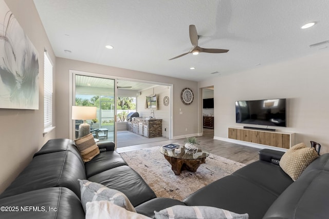 living room featuring ceiling fan, light hardwood / wood-style flooring, and a textured ceiling