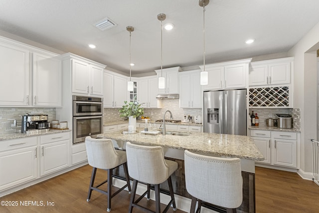 kitchen featuring pendant lighting, dark wood-type flooring, white cabinetry, stainless steel appliances, and an island with sink