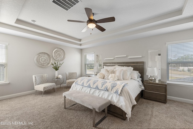 carpeted bedroom featuring ceiling fan, a tray ceiling, multiple windows, and a textured ceiling