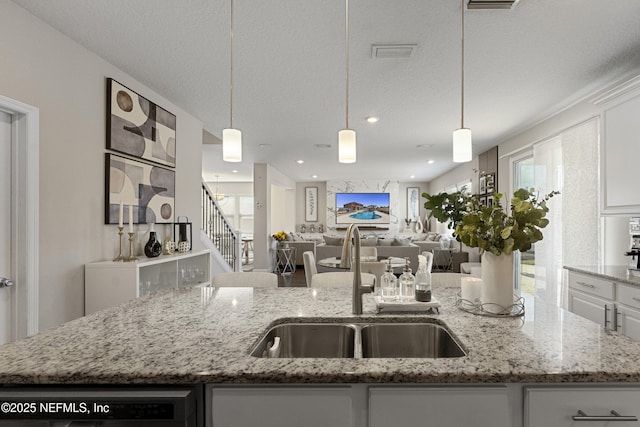 kitchen with pendant lighting, sink, a kitchen island with sink, and white cabinets