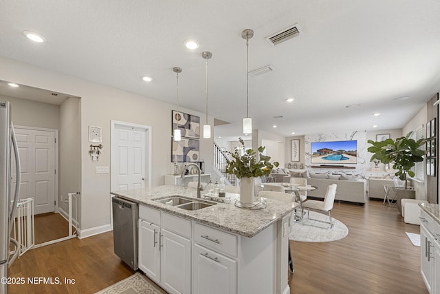 kitchen featuring white cabinetry, light stone counters, decorative light fixtures, a center island with sink, and stainless steel appliances