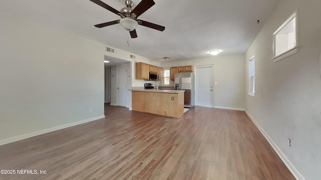 kitchen featuring light hardwood / wood-style flooring, ceiling fan, appliances with stainless steel finishes, a textured ceiling, and kitchen peninsula