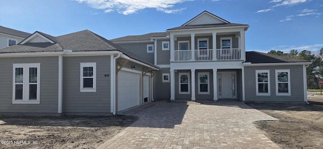 view of front of home featuring decorative driveway, roof with shingles, a balcony, and an attached garage