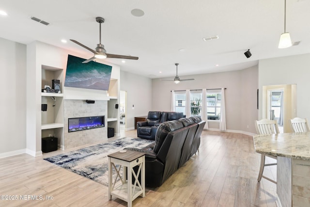 living room with built in shelves, ceiling fan, and light hardwood / wood-style flooring