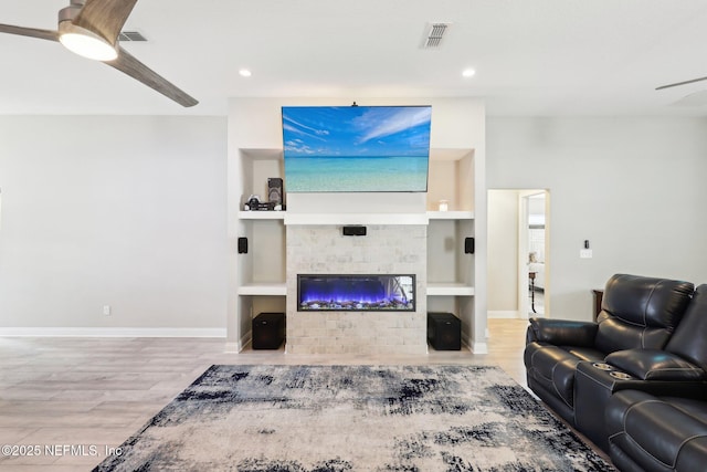 living room with wood-type flooring, a fireplace, built in features, and ceiling fan