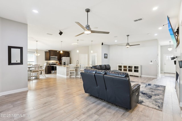 living room with ceiling fan, vaulted ceiling, and light wood-type flooring