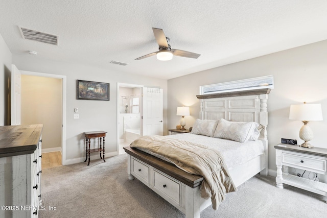 bedroom with ceiling fan, light colored carpet, connected bathroom, and a textured ceiling