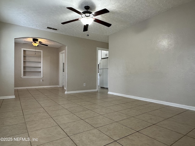 empty room with ceiling fan, built in shelves, light tile patterned floors, and a textured ceiling