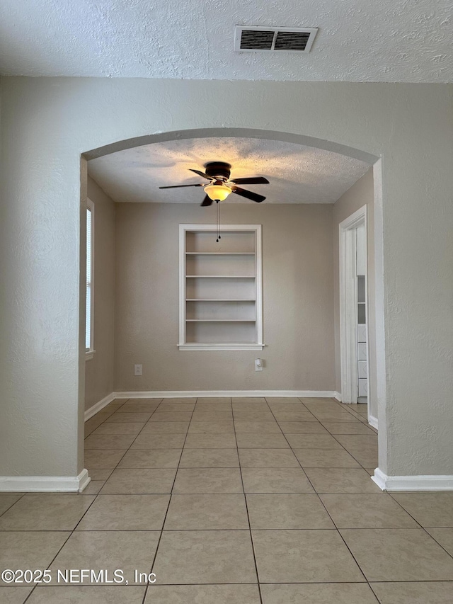 empty room with ceiling fan, light tile patterned floors, a textured ceiling, and built in shelves