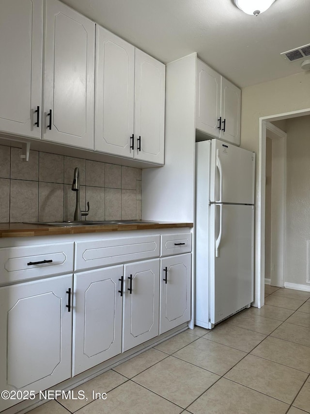 kitchen featuring tasteful backsplash, white cabinetry, white fridge, and light tile patterned flooring