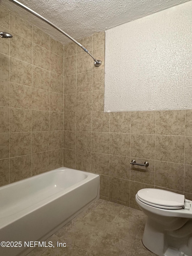 bathroom with tile patterned floors, toilet, tiled shower / bath, tile walls, and a textured ceiling