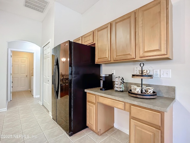 kitchen with light tile patterned floors, light brown cabinets, and black fridge