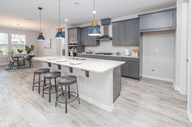 kitchen with sink, a center island with sink, pendant lighting, black gas cooktop, and wall chimney range hood