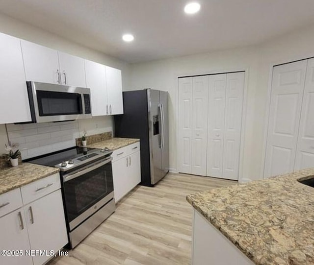 kitchen featuring light stone counters, appliances with stainless steel finishes, light hardwood / wood-style floors, and white cabinets