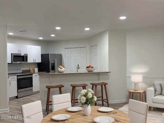 kitchen featuring appliances with stainless steel finishes, white cabinetry, a kitchen breakfast bar, light stone countertops, and light wood-type flooring