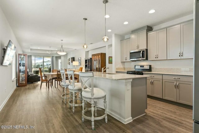 kitchen featuring stainless steel appliances, gray cabinets, hanging light fixtures, and a center island with sink