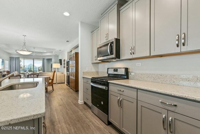 kitchen featuring sink, gray cabinetry, light stone counters, appliances with stainless steel finishes, and pendant lighting