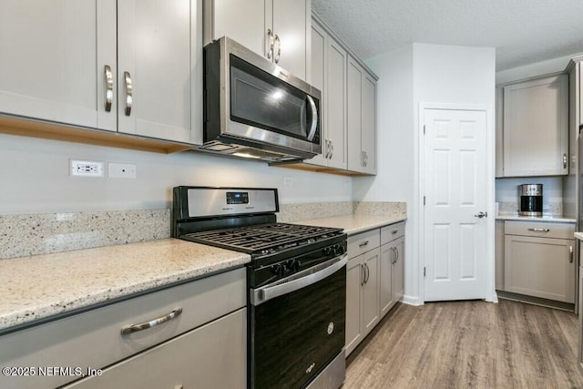 kitchen with stainless steel appliances, gray cabinetry, light stone counters, and light wood-type flooring