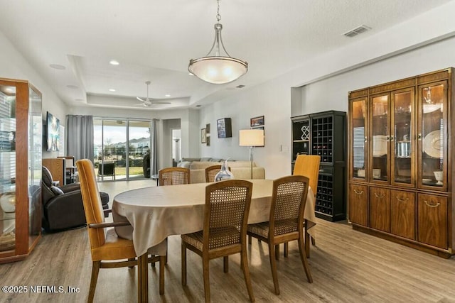 dining room with a raised ceiling, ceiling fan, and light wood-type flooring