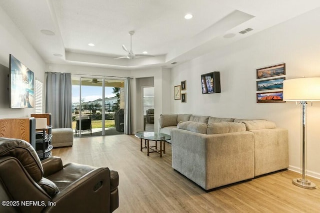 living room featuring hardwood / wood-style floors, a tray ceiling, and ceiling fan