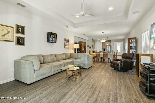 living room featuring hardwood / wood-style flooring, a raised ceiling, and ceiling fan