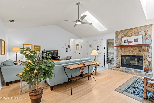 living room with ceiling fan, wood-type flooring, a fireplace, and lofted ceiling with skylight