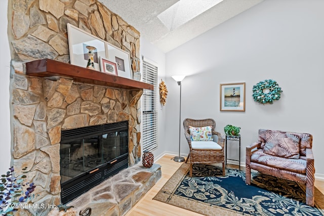 sitting room with hardwood / wood-style floors, vaulted ceiling with skylight, a fireplace, and a textured ceiling