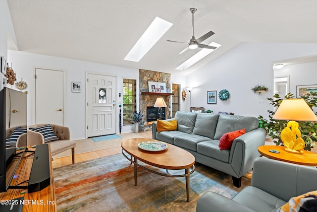 living room featuring hardwood / wood-style flooring, ceiling fan, a fireplace, and vaulted ceiling with skylight