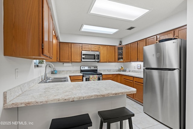 kitchen featuring light tile patterned flooring, sink, appliances with stainless steel finishes, a kitchen breakfast bar, and kitchen peninsula