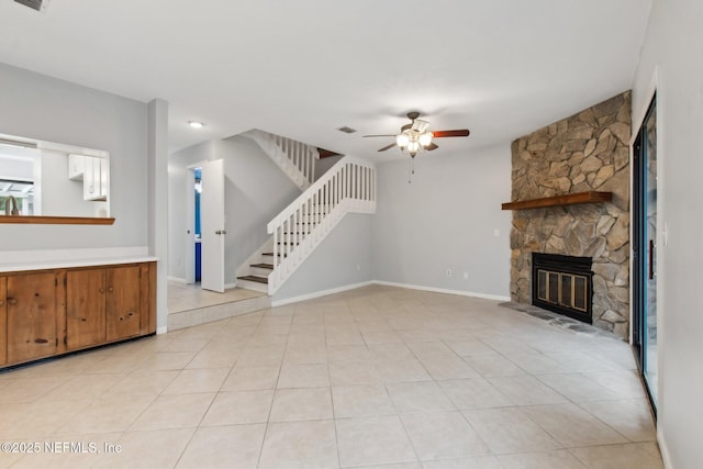 unfurnished living room with light tile patterned flooring, ceiling fan, and a stone fireplace