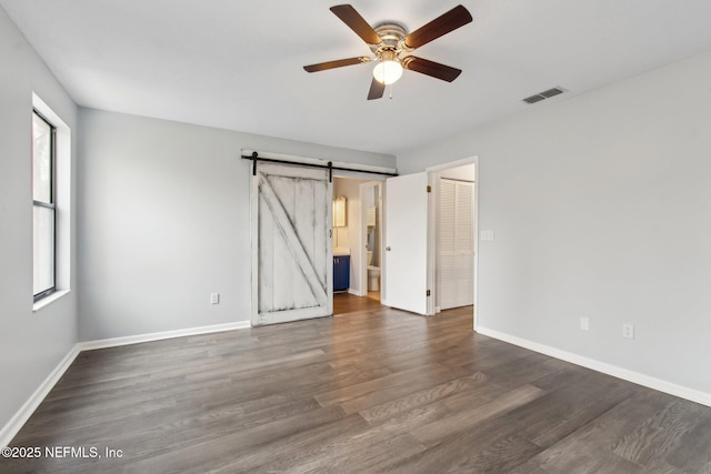 empty room featuring a barn door, dark hardwood / wood-style floors, and ceiling fan