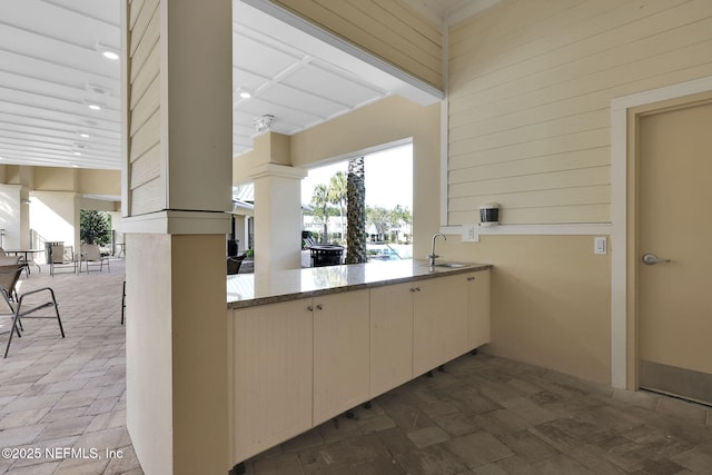 kitchen featuring a towering ceiling, light stone countertops, sink, and wood walls