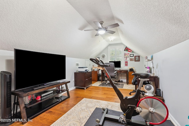 exercise room featuring ceiling fan, vaulted ceiling, light hardwood / wood-style floors, and a textured ceiling