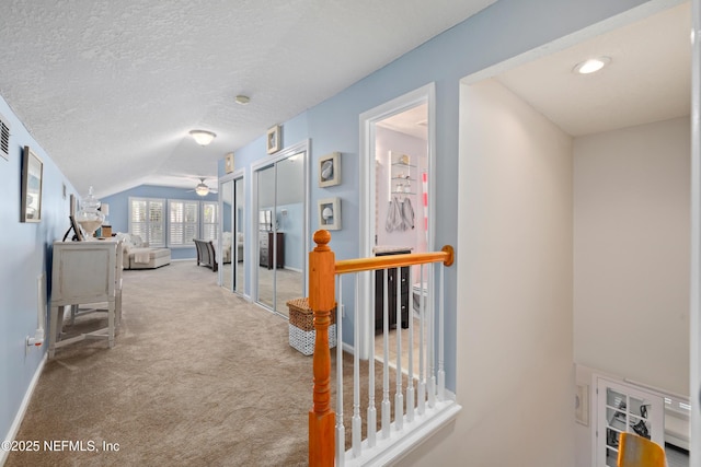 corridor with light colored carpet, vaulted ceiling, and a textured ceiling