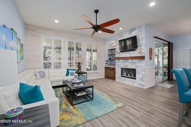 living room with a fireplace, built in features, ceiling fan, and light wood-type flooring