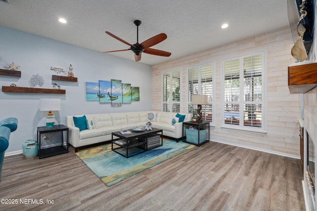 living room with ceiling fan, hardwood / wood-style floors, a textured ceiling, and a fireplace