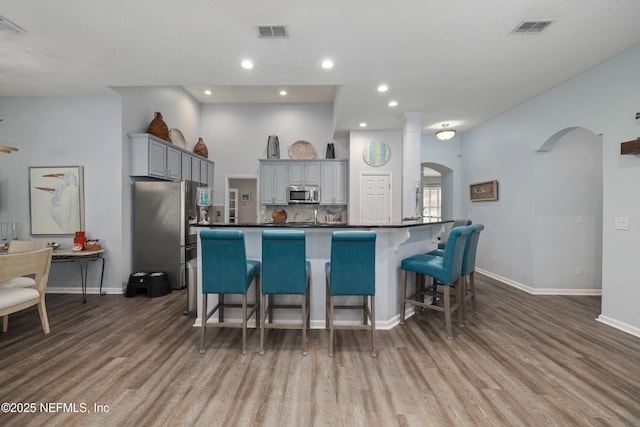 kitchen with a breakfast bar, stainless steel appliances, gray cabinets, and wood-type flooring