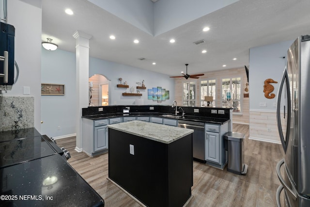 kitchen with a center island, light hardwood / wood-style flooring, appliances with stainless steel finishes, kitchen peninsula, and dark stone counters