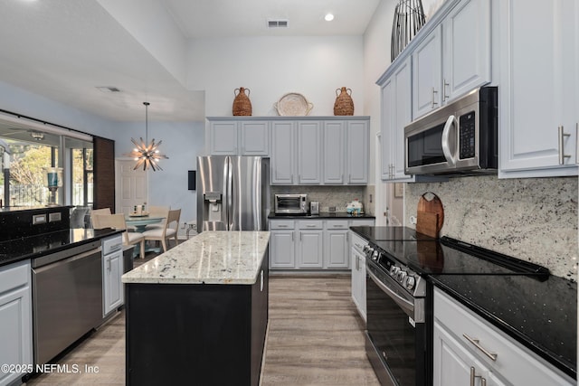 kitchen featuring tasteful backsplash, hanging light fixtures, appliances with stainless steel finishes, a kitchen island, and dark stone counters