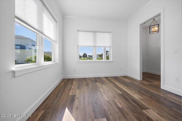 spare room featuring crown molding, a healthy amount of sunlight, dark hardwood / wood-style floors, and a notable chandelier