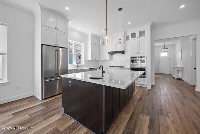 kitchen featuring sink, appliances with stainless steel finishes, white cabinetry, ornamental molding, and a center island with sink