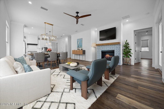 living room featuring a tiled fireplace, hardwood / wood-style flooring, ornamental molding, and ceiling fan