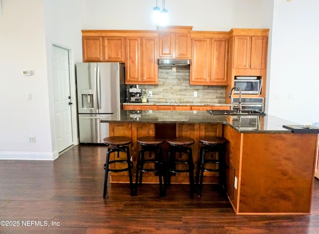 kitchen with tasteful backsplash, an island with sink, sink, stainless steel fridge, and dark wood-type flooring