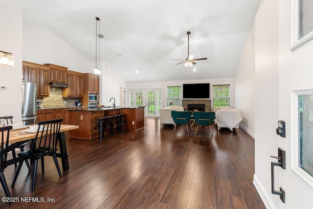 dining space featuring dark wood-style floors, a ceiling fan, high vaulted ceiling, a lit fireplace, and baseboards