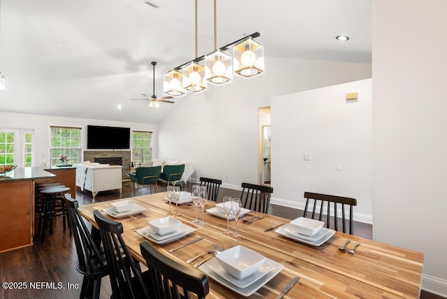 dining area featuring baseboards, dark wood finished floors, a ceiling fan, and a stone fireplace