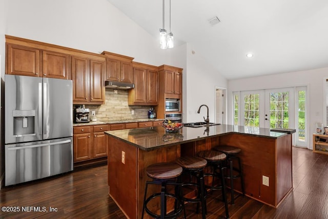 kitchen featuring stainless steel appliances, under cabinet range hood, a kitchen island with sink, and brown cabinets