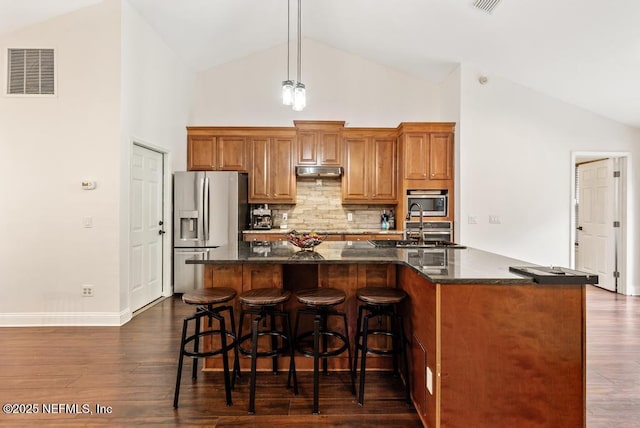 kitchen featuring visible vents, appliances with stainless steel finishes, dark wood-style floors, brown cabinetry, and a center island with sink