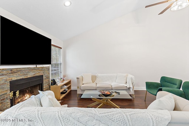 living room featuring lofted ceiling, dark wood-type flooring, a ceiling fan, a stone fireplace, and baseboards