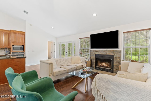 living room with light wood finished floors, visible vents, french doors, and a stone fireplace