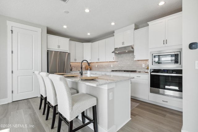 kitchen featuring appliances with stainless steel finishes, a center island with sink, and white cabinets